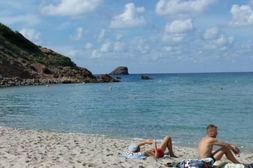 two people laying on the beach near the water at TRANQUILO APARTAMENTO con preciosa cala en la puerta in Ciutadella