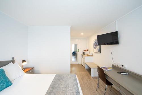 a bedroom with a bed and a desk with a television at New England Motor Lodge in Glen Innes