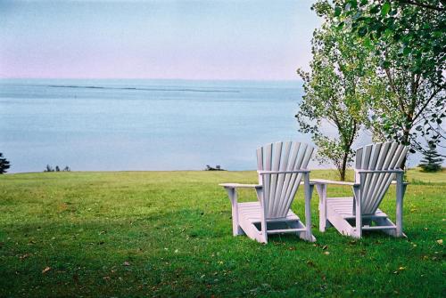 two chairs sitting in the grass near the water at Auberge De La Baie in Caraquet
