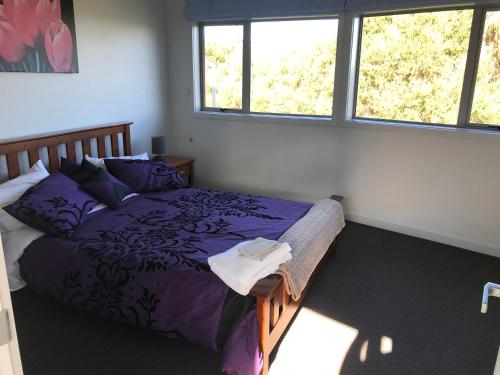 a bedroom with a bed with purple sheets and windows at Wilsons Retreat - Hosts On-site in Eskdale