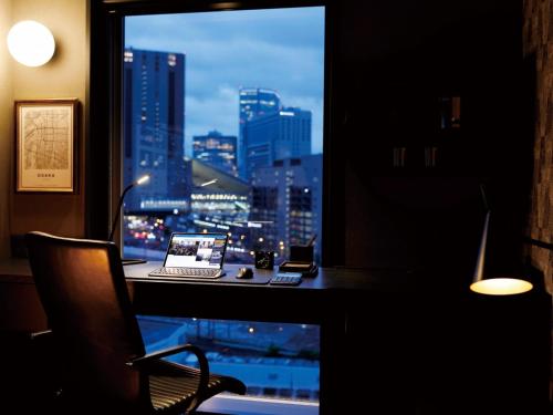 a desk with a laptop and a window with a city skyline at DEL style Osaka Shin Umeda by Daiwa Roynet Hotel in Osaka
