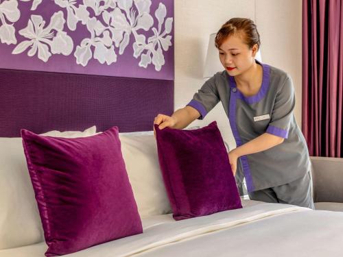 a woman putting purple pillows on a bed at Mercure Hai Phong in Hai Phong