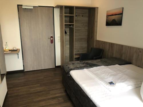 a bedroom with a bed and a chair and a door at WH Hotels Papenburg Zentrum in Papenburg