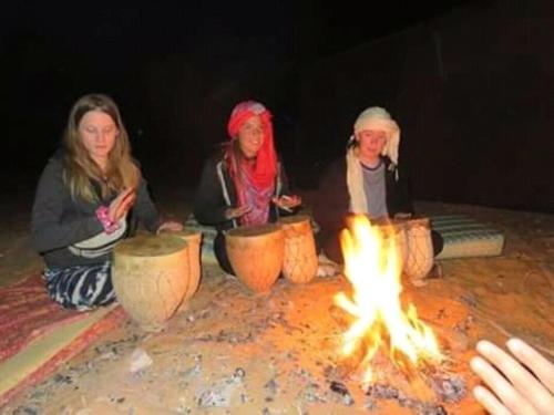 three women are sitting around a fire pit at RestCamp ErgChebbi in Merzouga