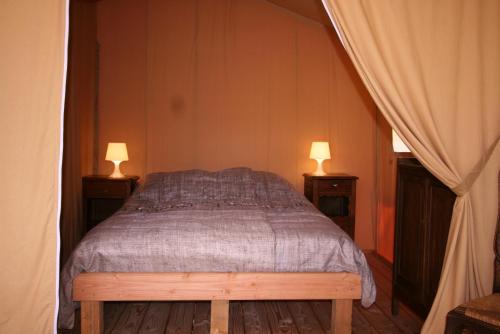 a bedroom with a bed with two lamps on both sides at Safaritent Les Pourettes in Feusines
