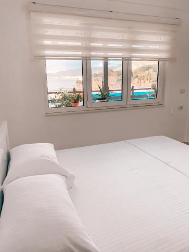 a white bedroom with a bed and a window at Aqua Holiday Apartments in Vlorë