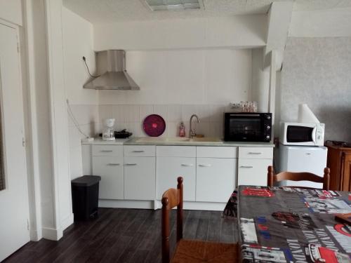 a kitchen with white cabinets and a table and a microwave at Chez charline in Sainte-Mère-Église