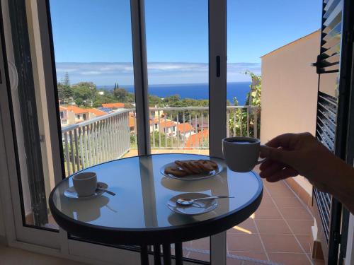 a person holding a coffee cup on a table on a balcony at Villa SCIROCCO Madeira - Ocean View in Machico