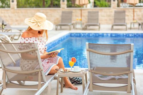 una mujer con sombrero sentada en una silla junto a una piscina en Luxury Apartments Queen en Petrovac na Moru