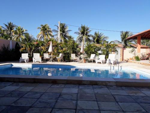 a pool with chairs and tables and palm trees at Villa Bianca Suítes in Beberibe