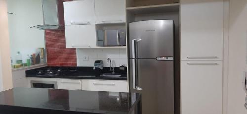 uma cozinha com um frigorífico de aço inoxidável e armários brancos em Apartamento Enseada LC01 no Guarujá