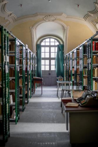 a library with shelves of books with a window at Il Seminario in Alba
