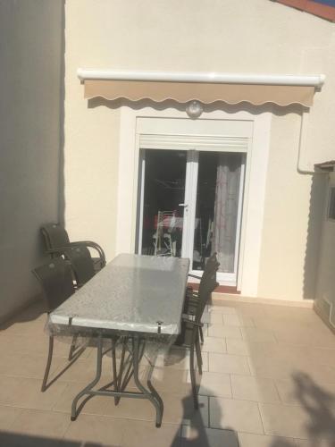 une table et des chaises sur une terrasse avec une fenêtre dans l'établissement Marendes Des Palombes 2, au Barcarès