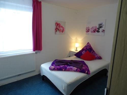 a small bedroom with a white bed with purple pillows at Gästehaus Uezel in Friedrichshafen
