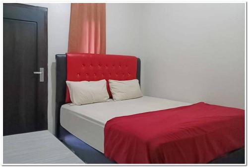 uma cama com uma cabeceira vermelha ao lado de uma porta em Hotel Dheadita Syariah Sungai Penuh Mitra RedDoorz em Sungaipenuh