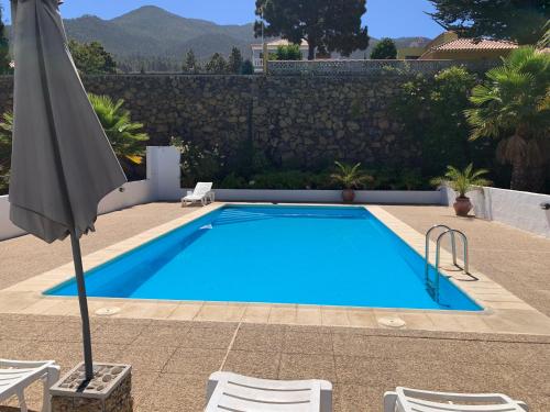 a blue swimming pool with an umbrella and chairs at Villas Las Cercas in El Paso