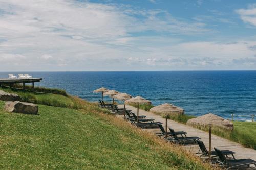 a row of chairs and umbrellas next to the ocean at Santa Barbara Eco-Beach Resort in Ribeira Grande