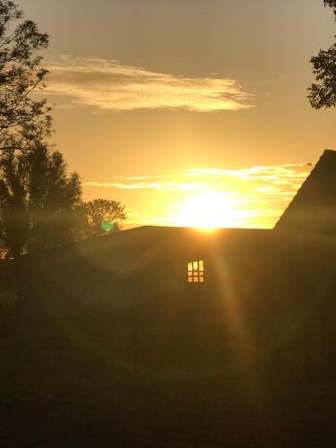 a sunset over a field with the sun setting behind a house at familieverblijf De groene Specht in Sluis