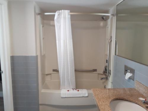 a bathroom with a shower with a white shower curtain at Travelodge by Wyndham Virginia Beach Bay Beach in Virginia Beach