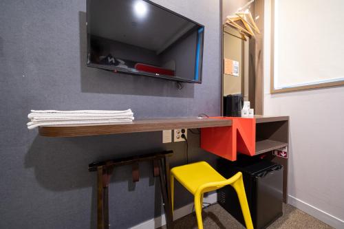 a desk with a tv on a wall with a yellow stool at Seoul N Guesthouse Dongdaemoon in Seoul