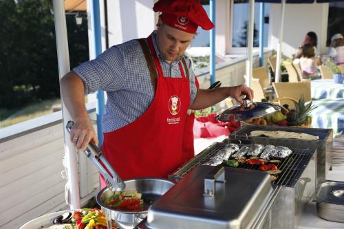 a man in a red apron preparing food on a grill at Familotel Mein Krug in Warmensteinach