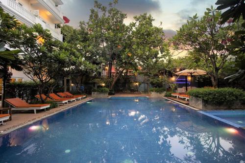 a swimming pool in a hotel with chairs and trees at Amber Angkor Villa Hotel & Spa in Siem Reap