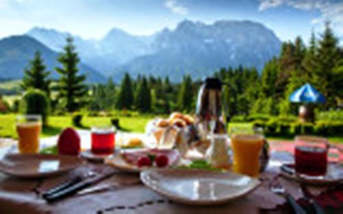 a table with plates of food on it with mountains in the background at Bäckeralm© - B&B 16 + in Mittenwald