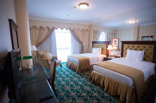 a hotel room with two beds and a chair at Habitat All Suites, Al Khobar in Al Khobar