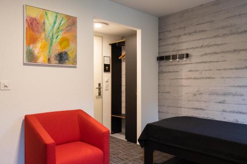 a bedroom with a red chair and a painting on the wall at B&B Hotel Mattli Übernachtung Frühstück in Morschach
