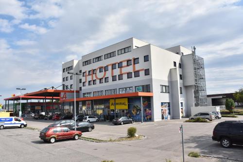 ein großes weißes Gebäude mit Autos auf einem Parkplatz in der Unterkunft HB1 Budget Hotel - contactless check in in Wiener Neudorf