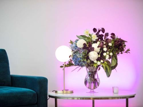 a vase of flowers on a table next to a lamp at Mercure Canberra Belconnen in Canberra