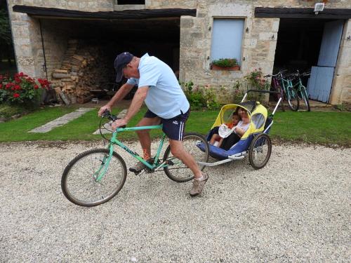 Ein Mann, der mit einem Kind in einem Wagen ein Fahrrad schiebt in der Unterkunft Le Petit Moulin Tournesol BnB in Sainte-Soline