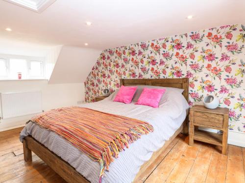 una camera da letto con letto dotato di cuscini rosa e carta da parati floreale di Bridge End Cottage a Norwich