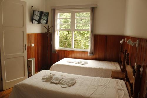 two beds in a room with a window at Hotel Casa São José in Campos do Jordão