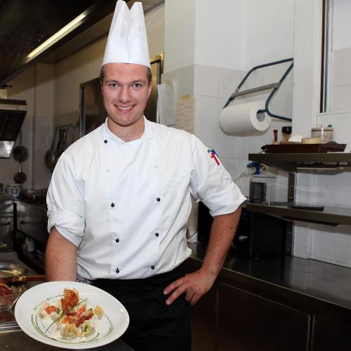 a chef holding a plate of food in a kitchen at Park Hotel Arnica in Falcade