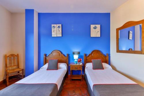 2 camas en una habitación con una pared azul en Hostal Alfonso XI en Guadalupe