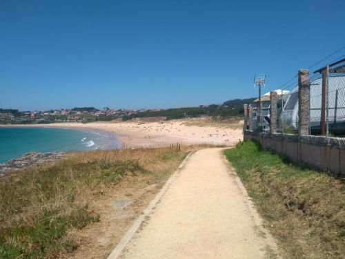 a dirt road next to a beach with a fence at Camping Paxariñas in Portonovo