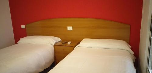 two beds in a room with red walls at Hostal Meson de Paco in Cariñena