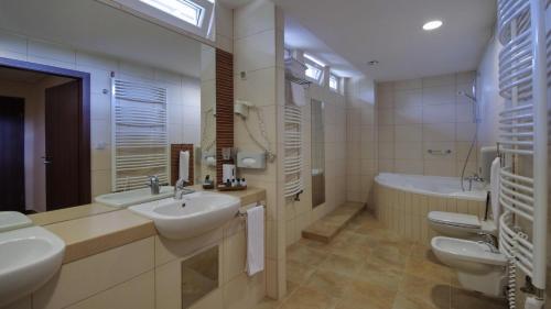 ein Badezimmer mit zwei Waschbecken, einer Badewanne und zwei WCs in der Unterkunft Wellness Hotel Gyula in Gyula
