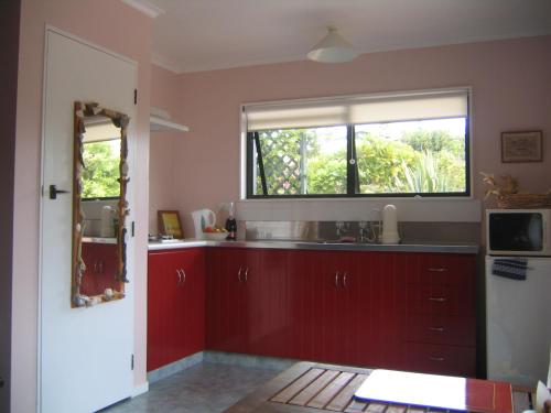una cocina con armarios rojos y una ventana en Moanarua Beach Cottage, en Ohope Beach