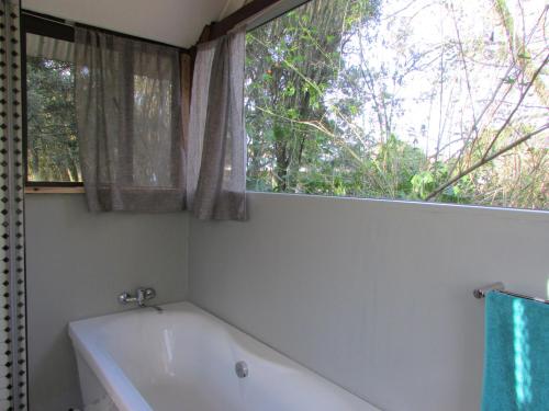 baño con bañera blanca y ventana en Old Pine Cabin Karkloof en Karkloof Nature Reserve