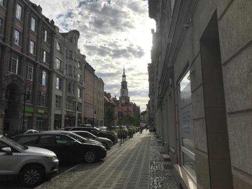 una calle de la ciudad con coches aparcados y una torre del reloj en Mungo Jerry Studio Apartment in the Old Town en Poznan