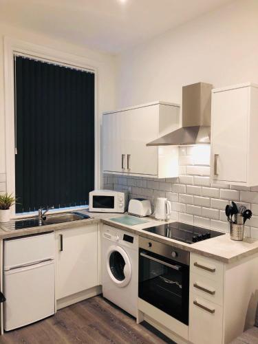 a kitchen with white cabinets and a washer and dryer at Albert Hottub & Jacuzzi Apartments in Blackpool