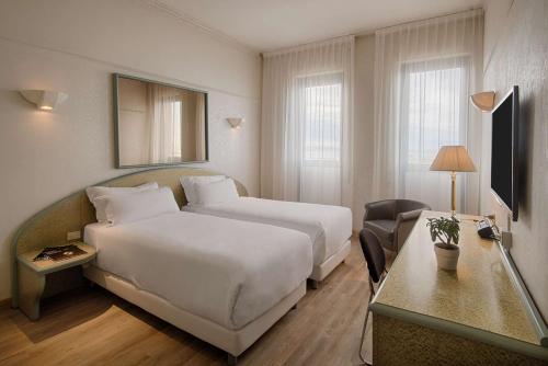 Habitación de hotel con cama blanca grande y escritorio. en NH Ancona en Ancona