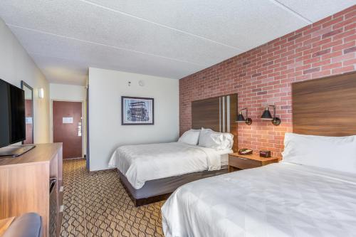 a hotel room with two beds and a flat screen tv at Burrstone Inn, an Ascend Collection Hotel in Utica
