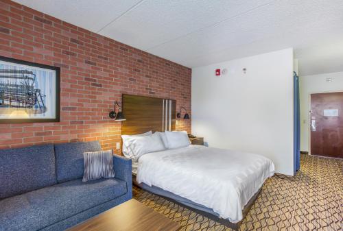 a bedroom with a bed and a couch and a brick wall at Burrstone Inn, an Ascend Collection Hotel in Utica