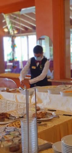 una mujer con una máscara de cara parada detrás de una mesa con comida en Hotel Diana, en San Zeno di Montagna