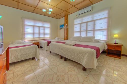 a bedroom with three beds and two windows at Hotel San Vicente Galapagos in Puerto Villamil
