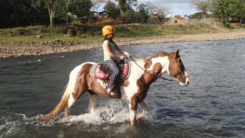a woman riding a horse in the water at La Finca Lodge in Fortuna
