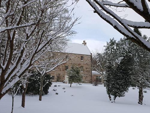 a snow covered yard with a building and trees at The Old Millhouse - Luxury Retreat with Sauna, Cold Plunge, Yoga & Swim SPA in Dalkeith